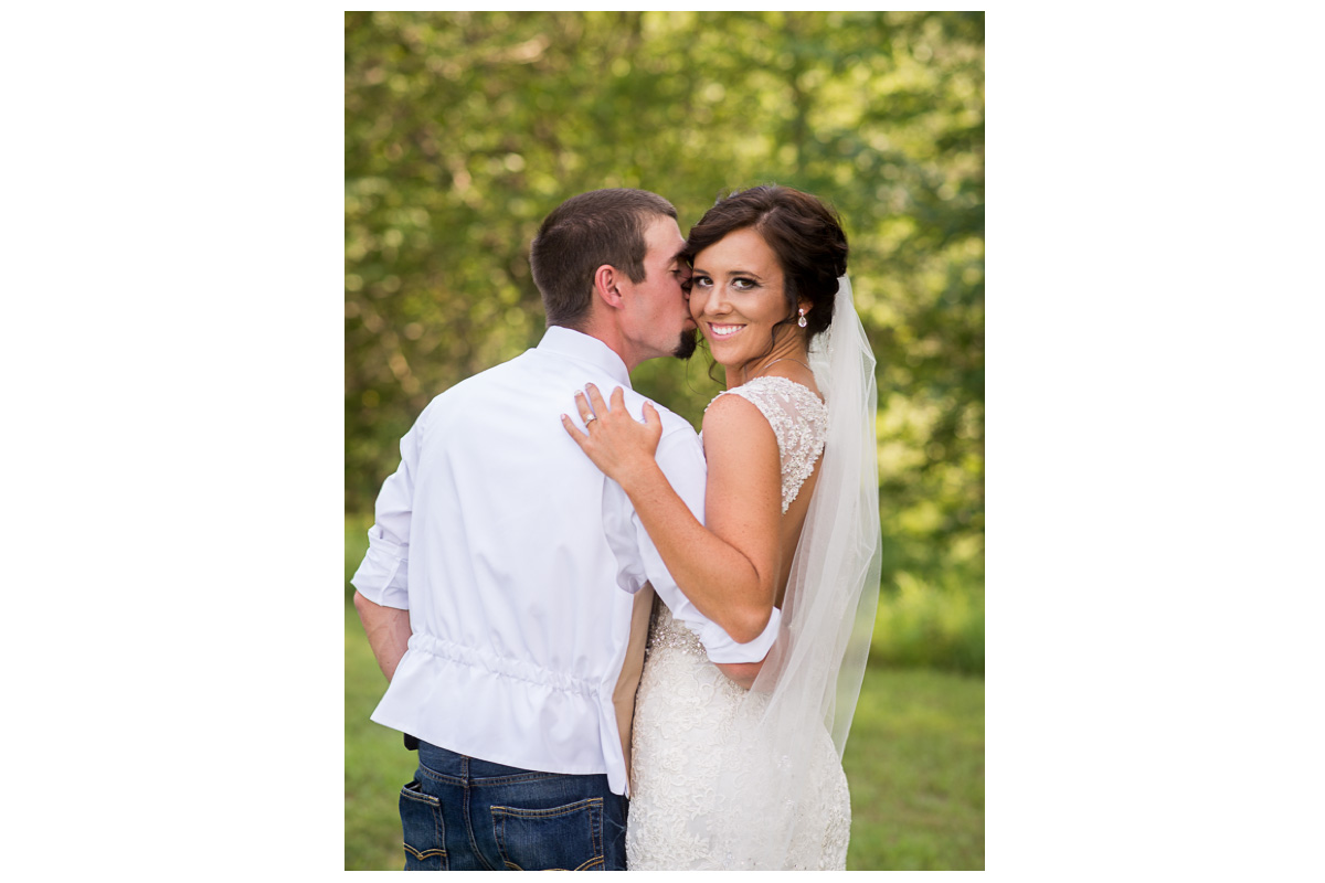 groom kissing bride's check at farm wedding