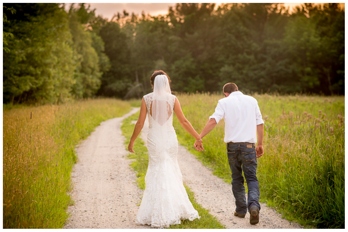 bride and groom walking hand in hand at sunset on dirt road