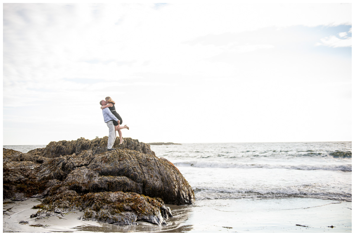 couple standing on rock in ocean for engagement photos