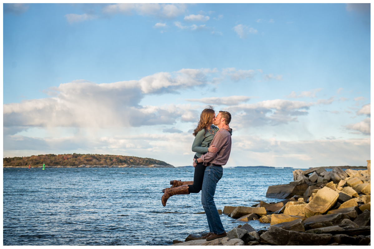 engaged couple kissing next to the ocean on rocks in cape elizabeth