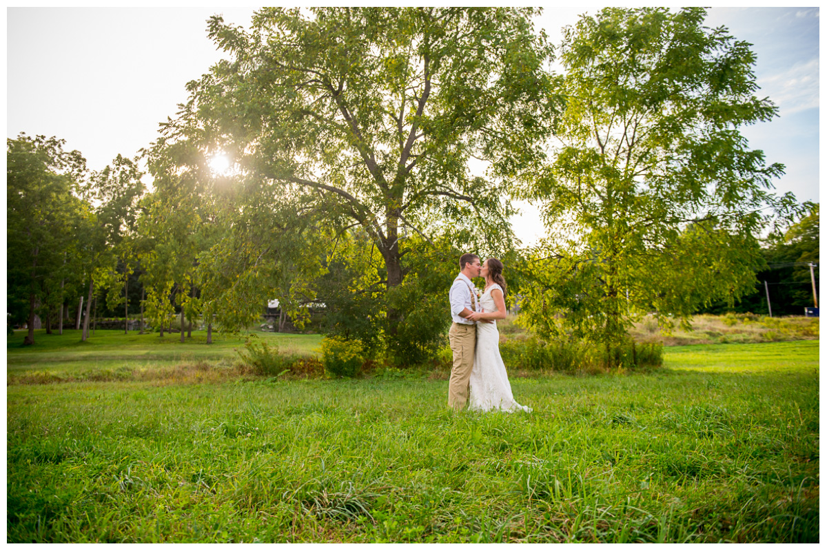 bride and groom kissing near trees in a field in new hampshire