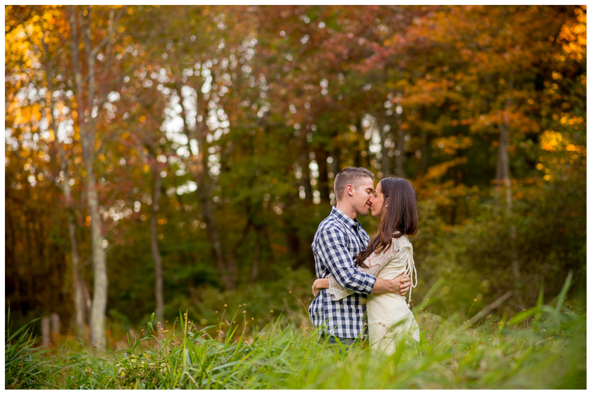 couple kissing in field with orange and red leaves