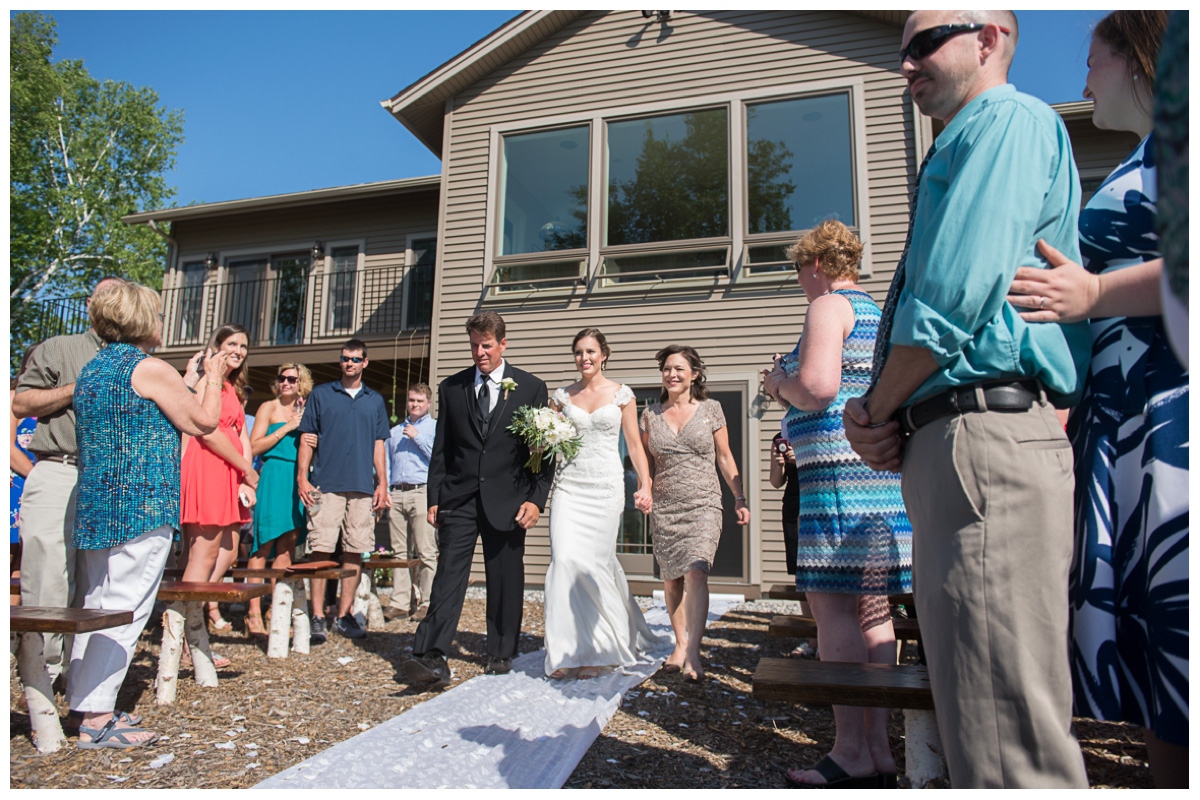 Bride walking down the aisle with parents at an outside wedding