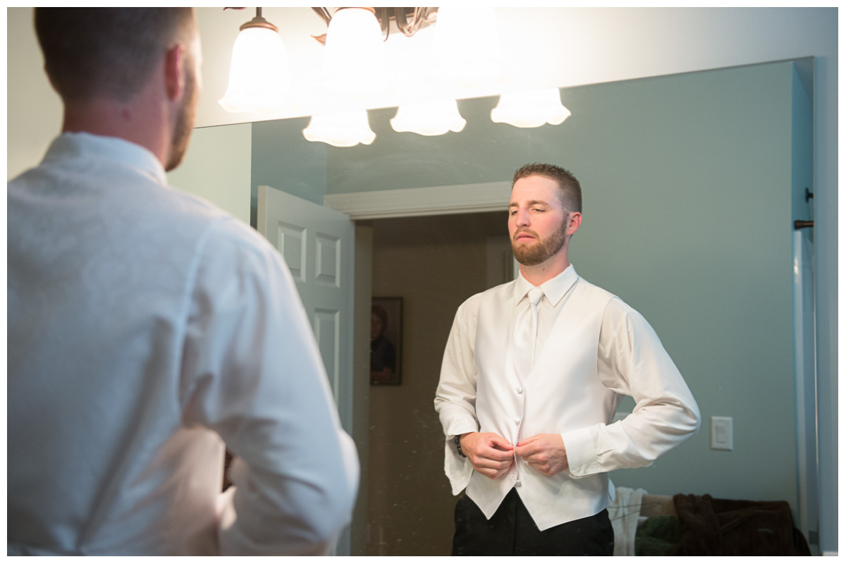 Groom looking in mirror getting ready for wedding