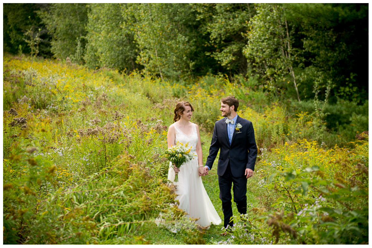 Bride and groom walking through wild flowers in Vermont