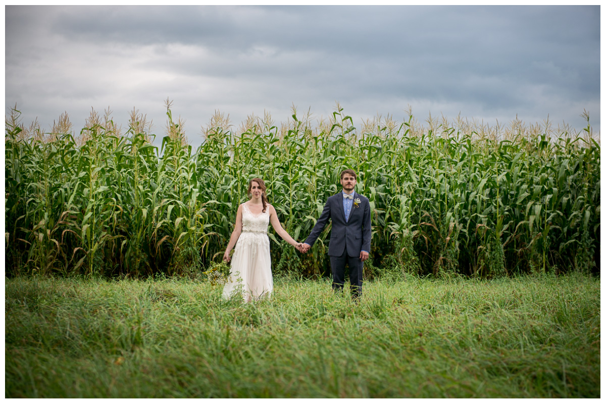 bride and groom holding hands in a field with storm clouds 