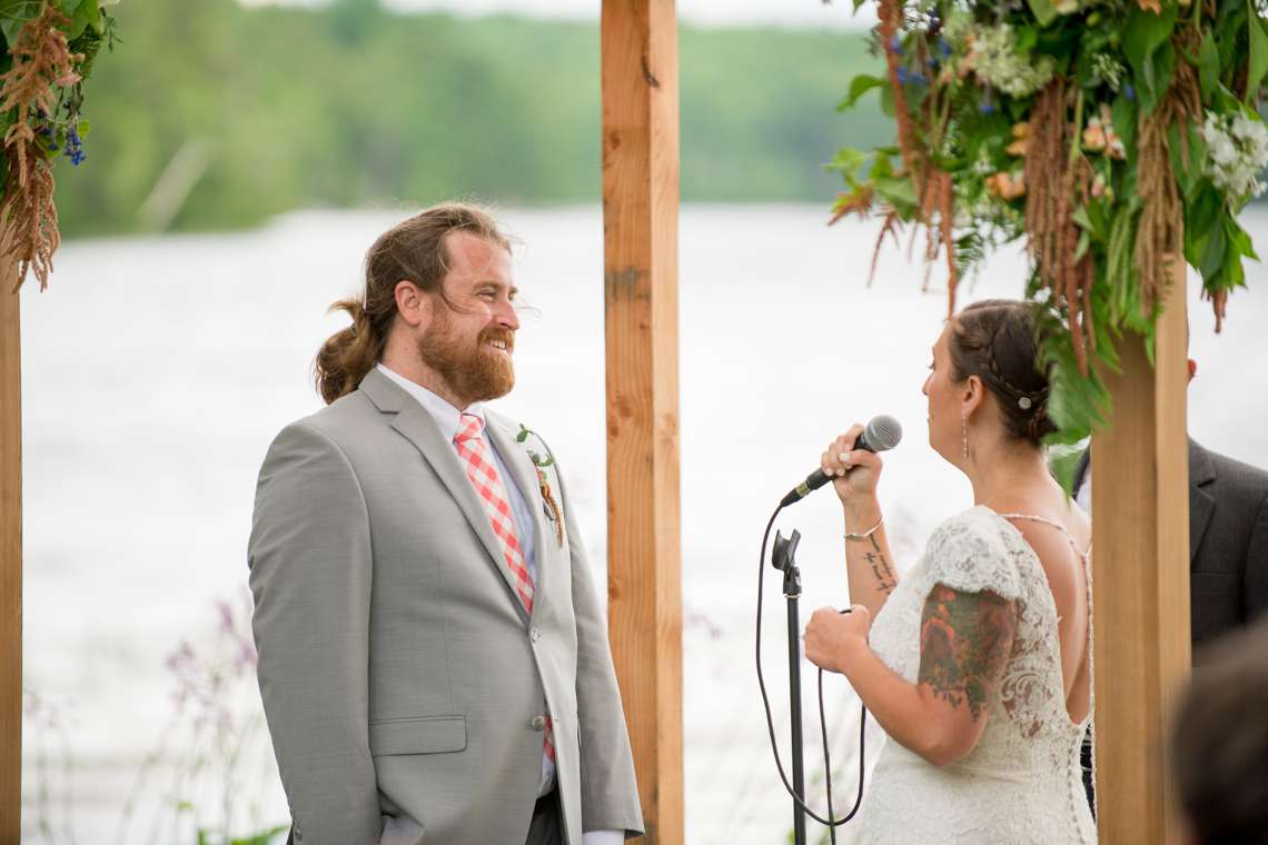 Groom smiling at bride during wedding ceremony at a lake