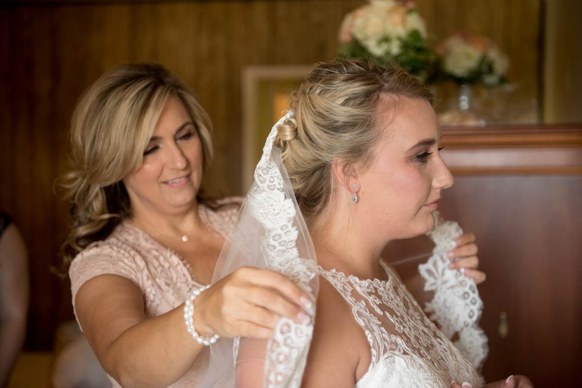 mother of bride putting veil on bride before rustic wedding ceremony