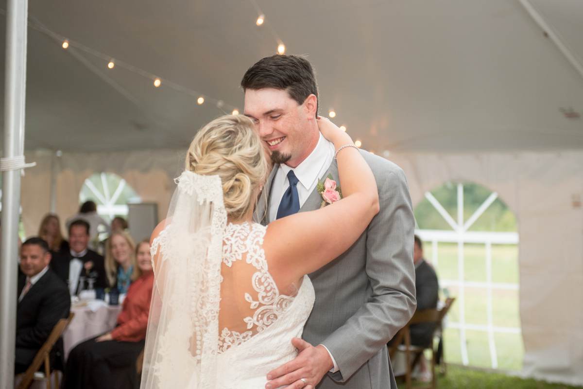 bride and groom first dance under lights in white tented reception