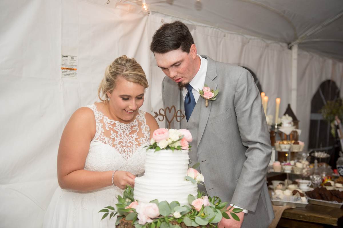 backyard tented reception, bride and groom cutting rustic themed wedding cake